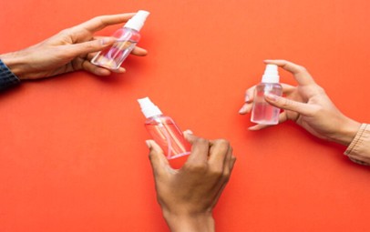 3 people are holding small sanitizer spray bottles in their hands.